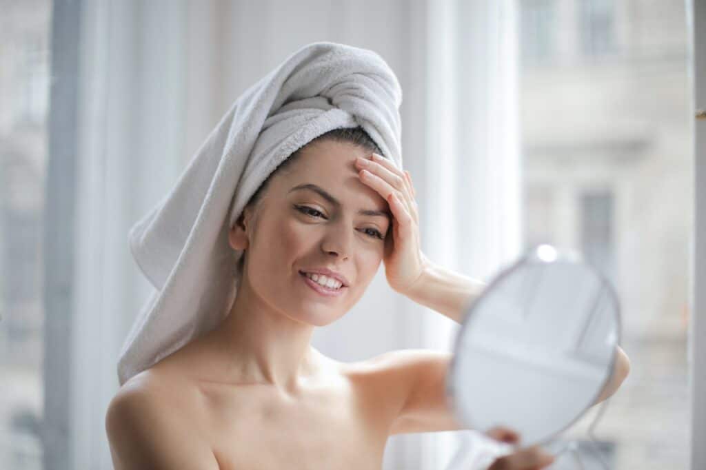 Young woman looks at her face in the mirror after a bath