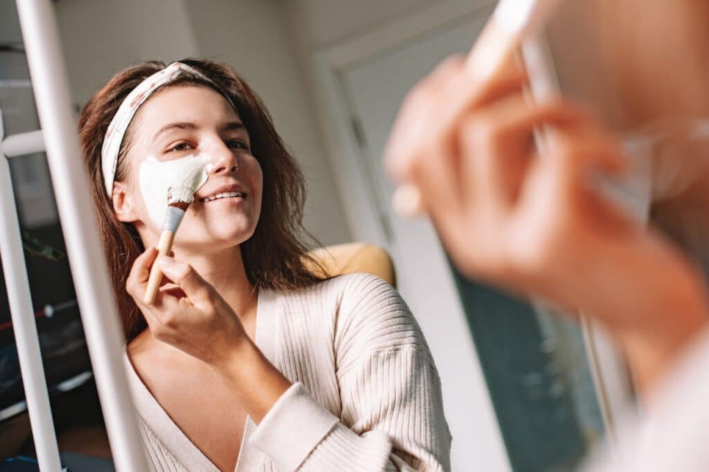 Woman Looking in Mirror Applying Face Mask As A Part Of Korean Skin Care Routine